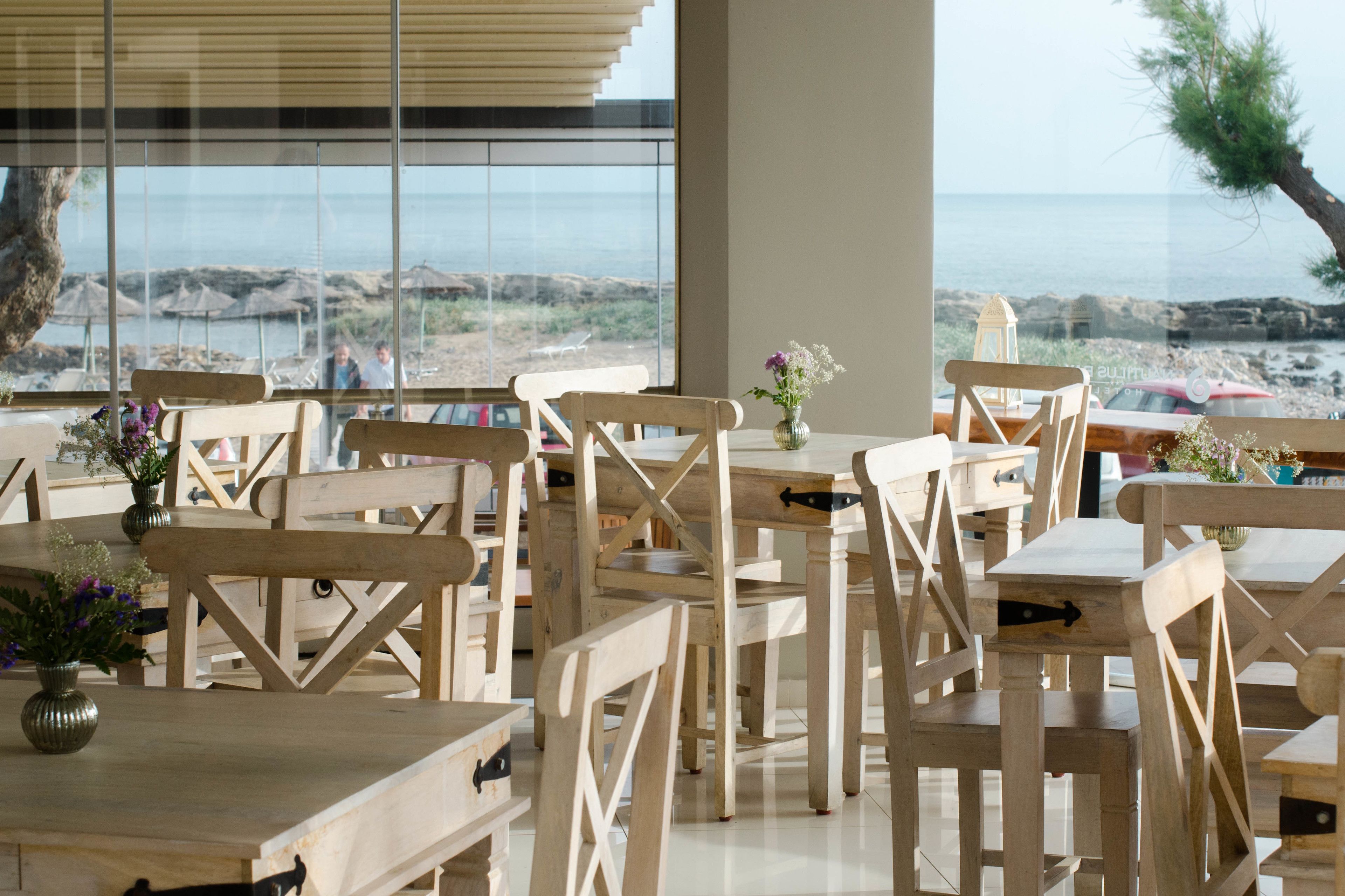 A wooden dining area with tables and chairs, large windows with a view of the beach and ocean.