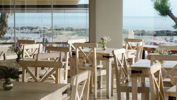 A wooden dining area with tables and chairs, large windows with a view of the beach and ocean.