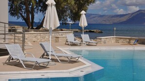 Zona de piscina con sillones y sombrillas, un muro de piedra y vistas al mar y a las montañas.