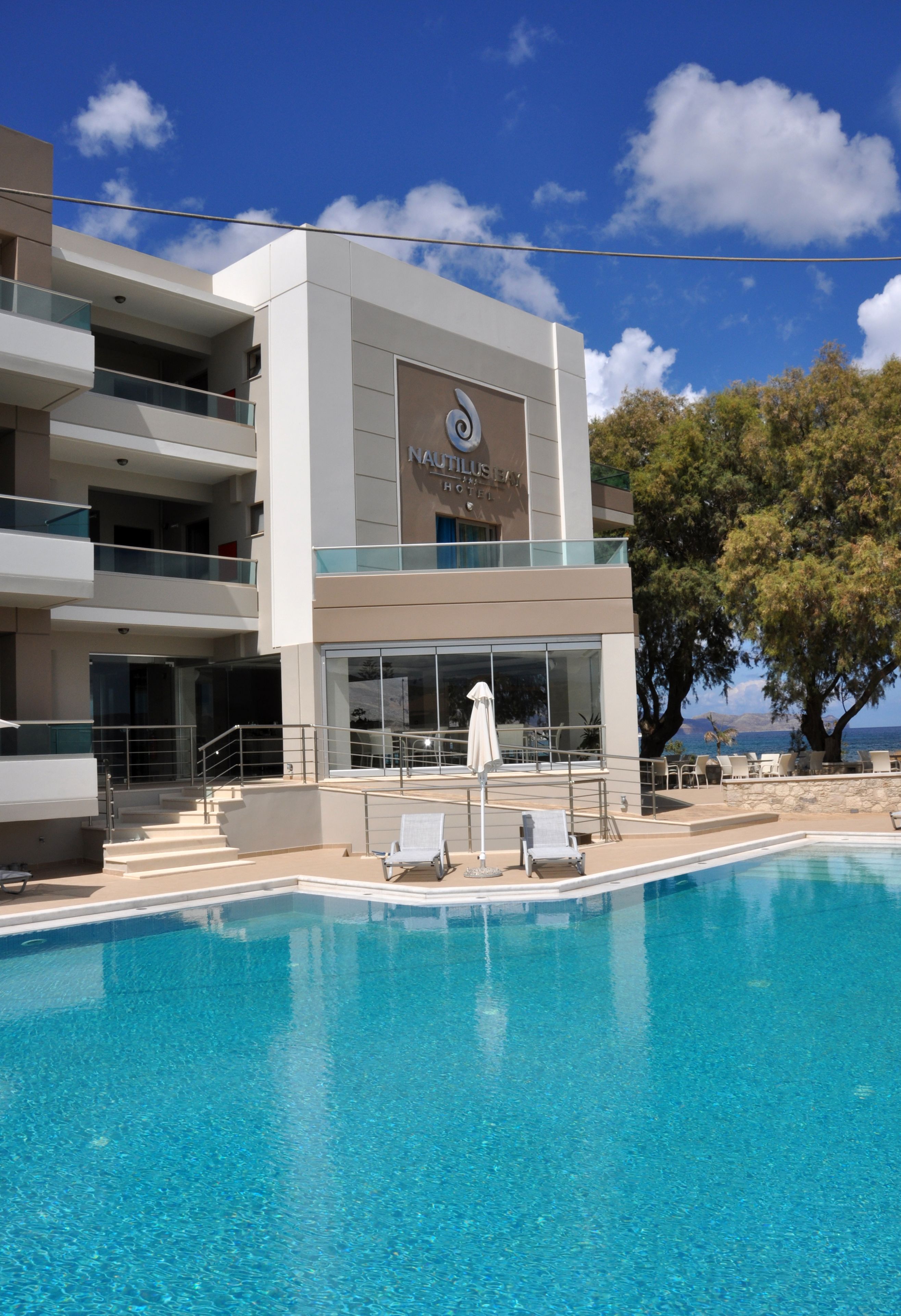 Un hotel modern amb piscina, zona de seients a l'aire lliure i vista al mar.