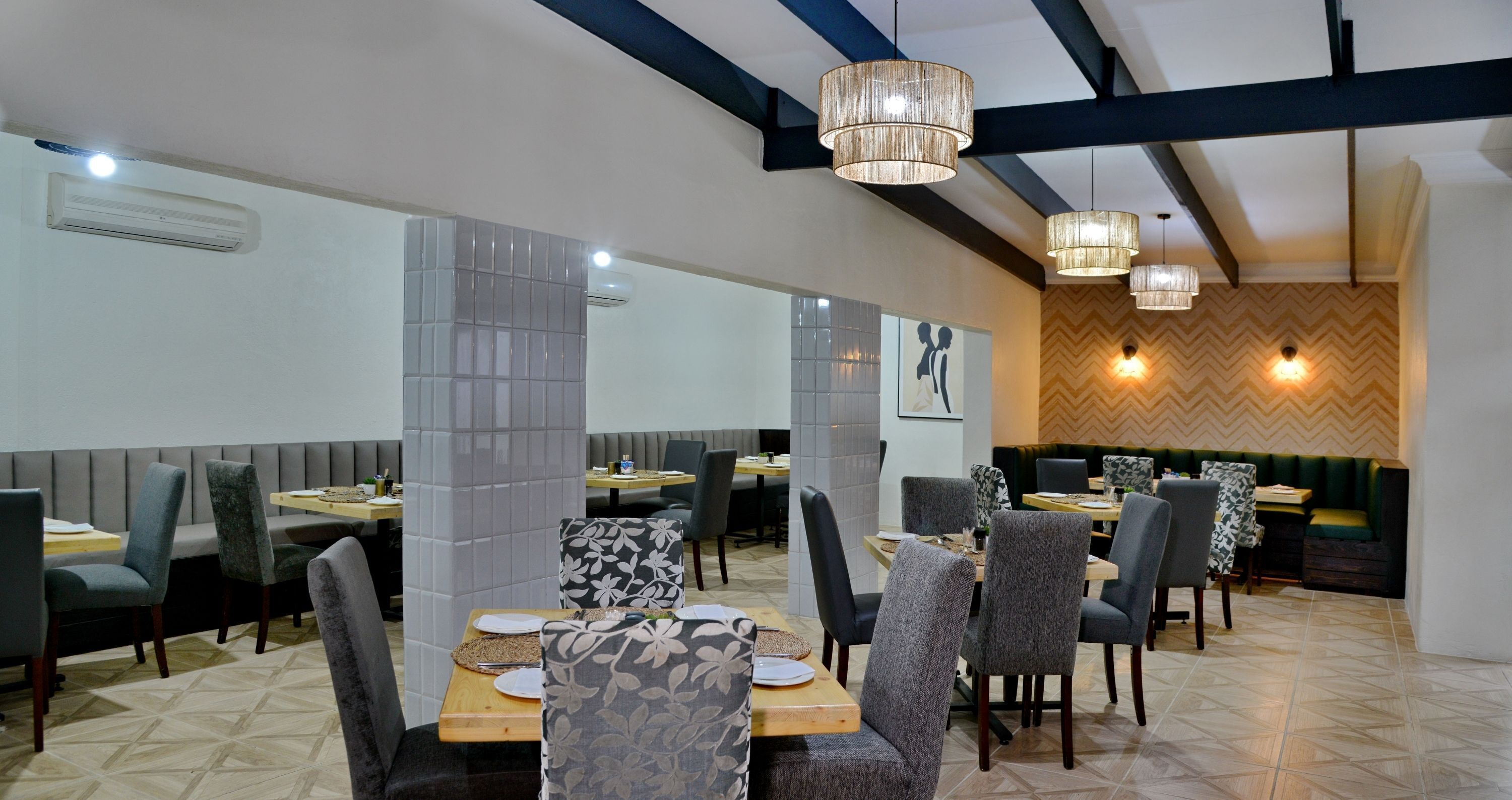 A restaurant with multiple dining tables and chairs, a patterned wall, and hanging pendant lights.