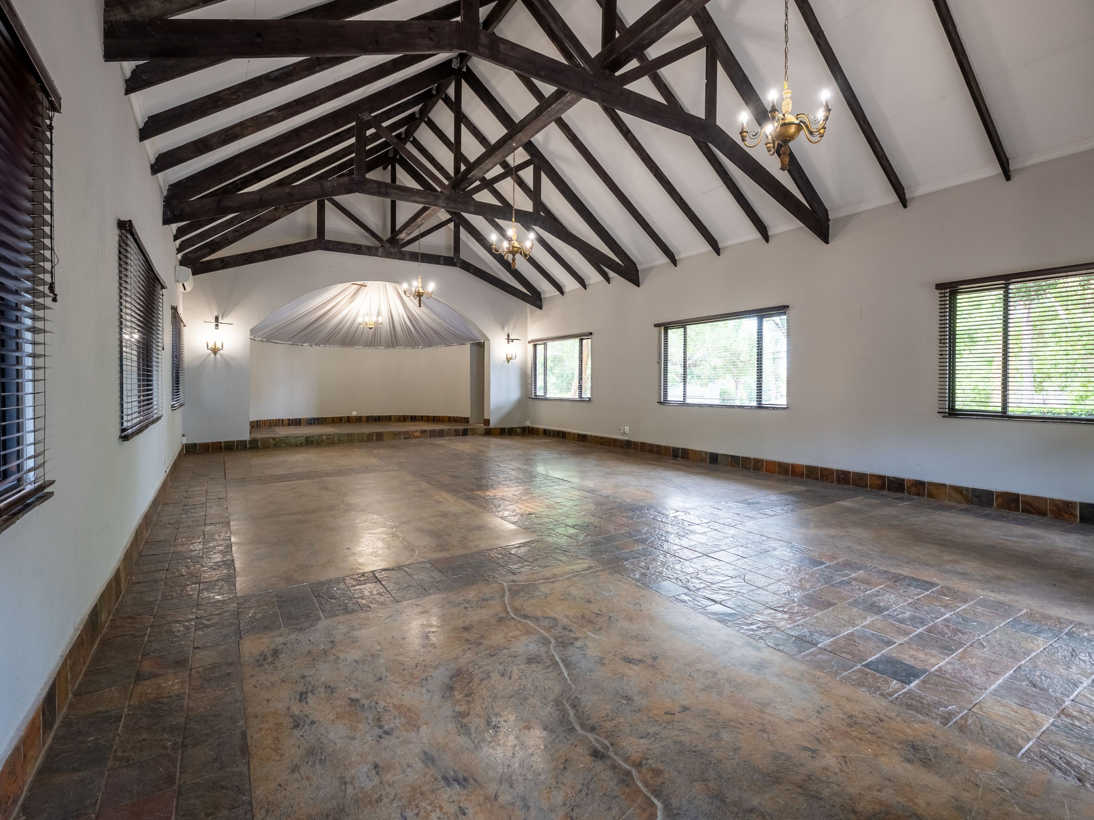 A spacious room with a high ceiling, exposed wooden beams, and large windows.