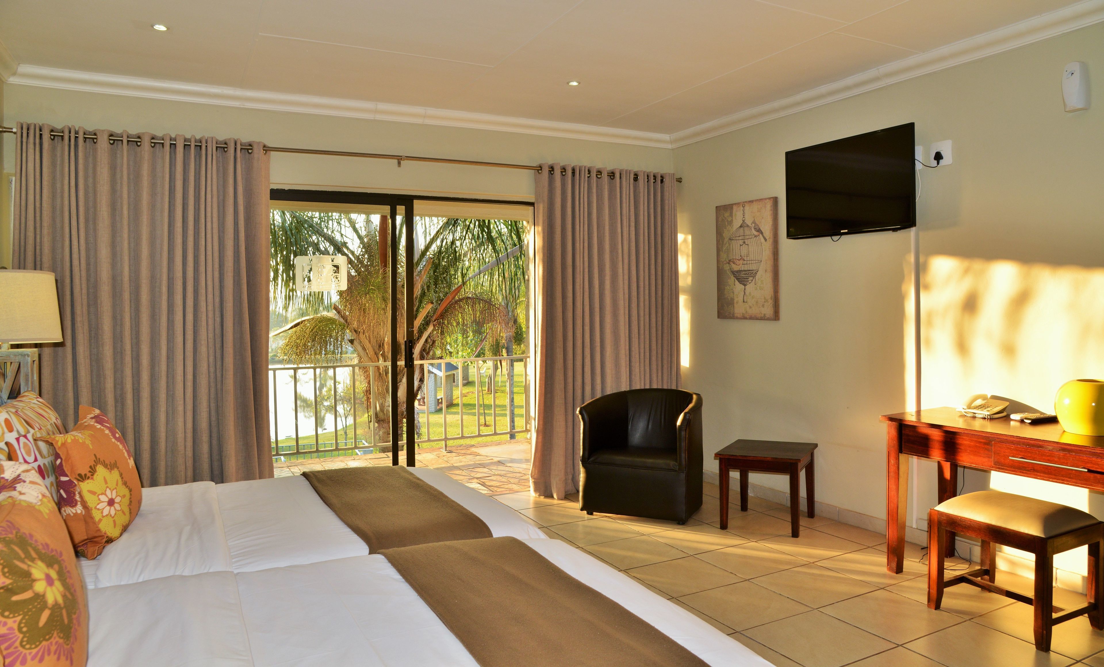 A hotel room with a bed, a desk, a chair, a TV, and a balcony with curtains.