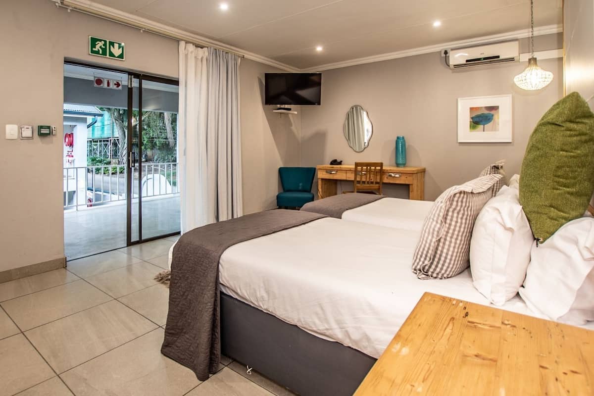 A hotel room with a bed, a desk, a chair, a TV, and an air conditioning unit.