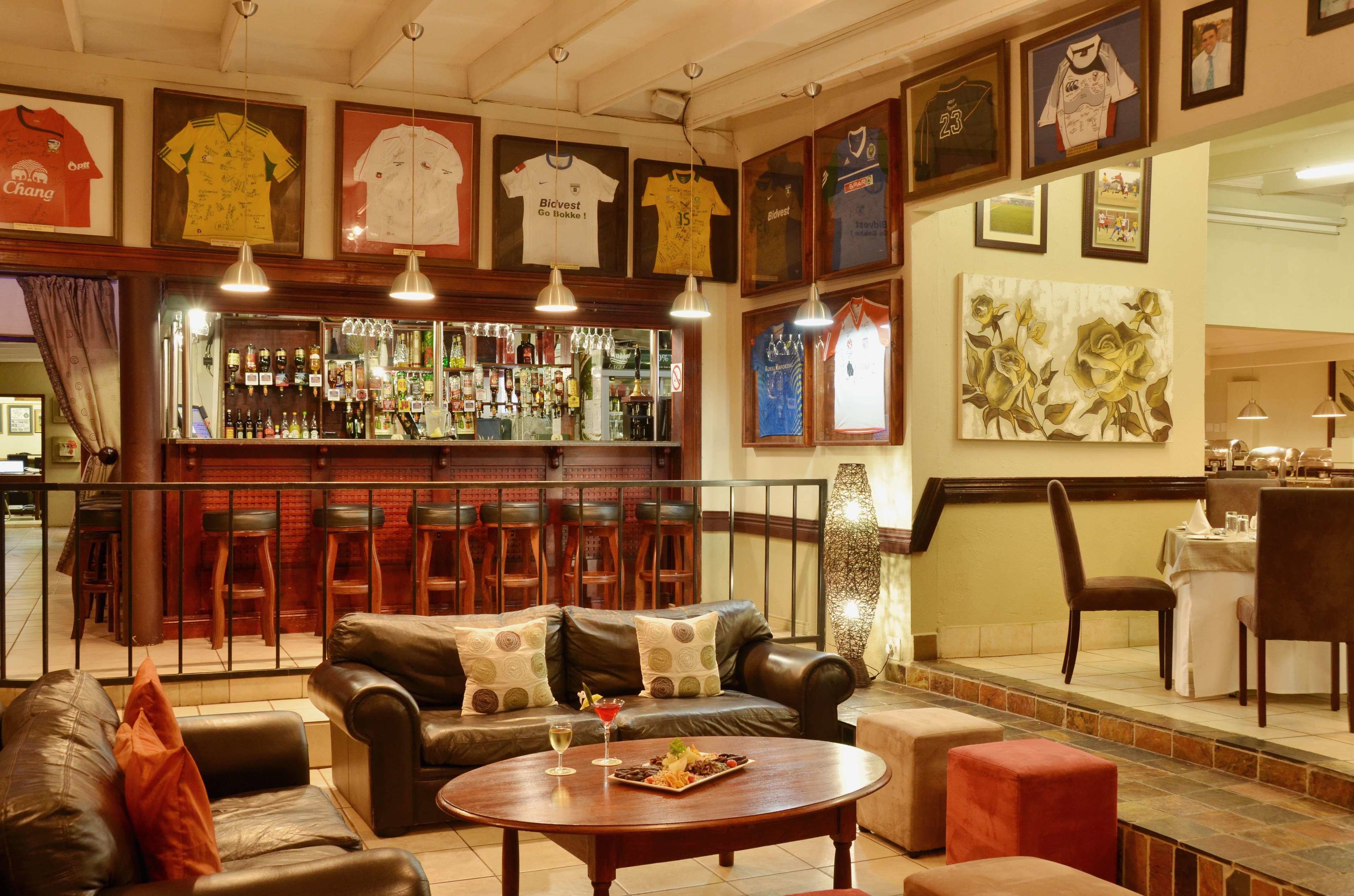 A bar area with leather seating, a bar counter with bottles, and framed sports jerseys on the wall.