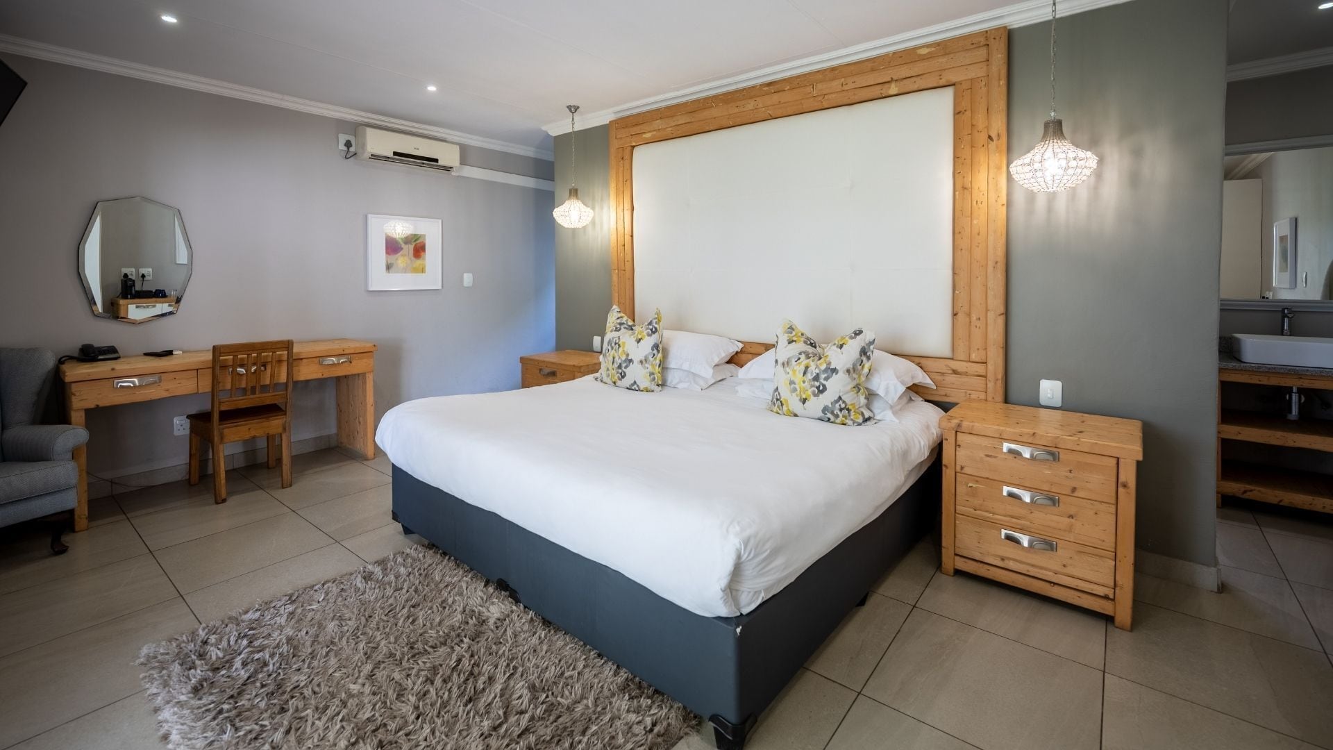 A bedroom with a large bed, wooden headboard, bedside tables, a desk, and a chair.
