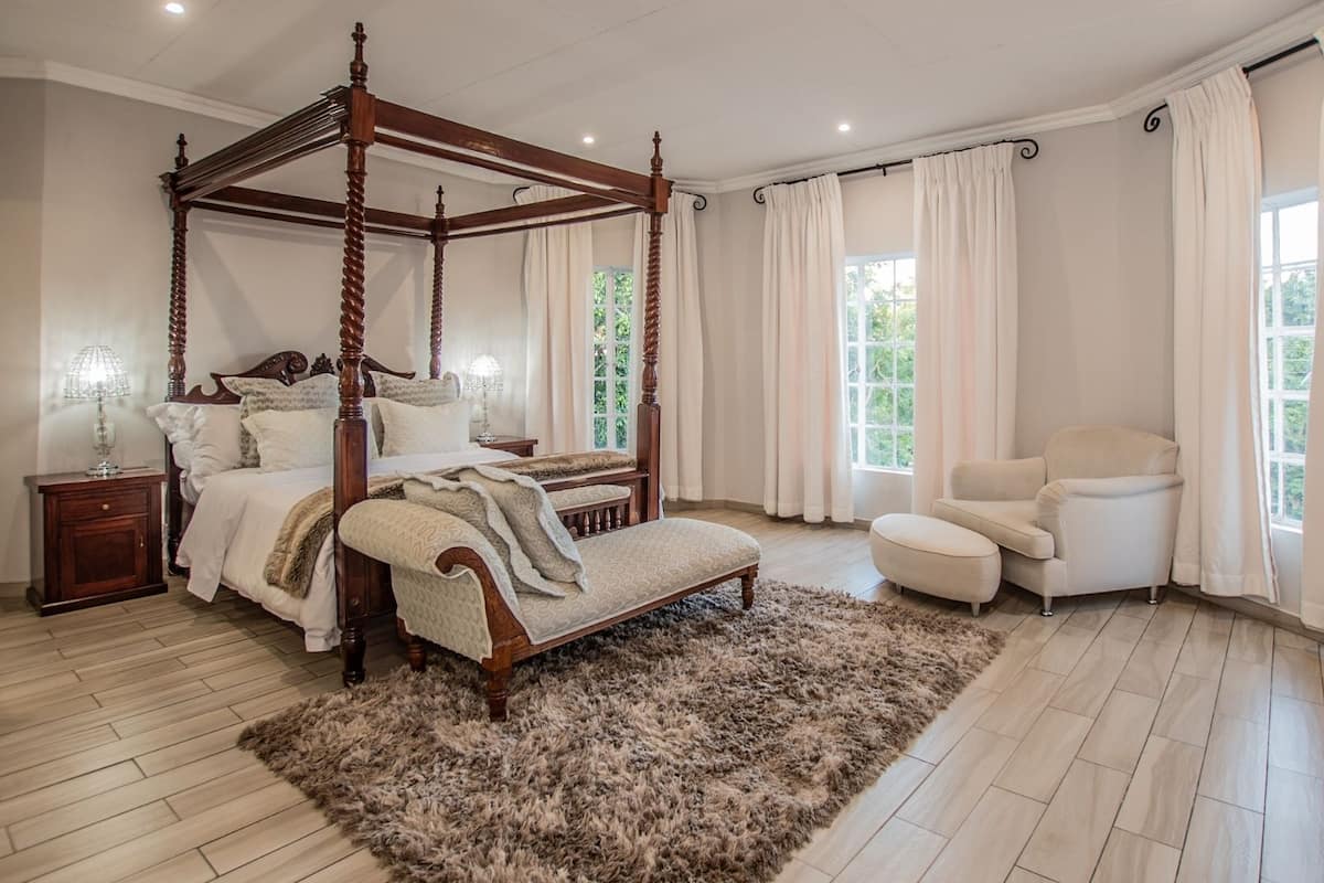 A spacious bedroom with a four-poster bed, a sitting area with a chair, and a large window providing natural light.