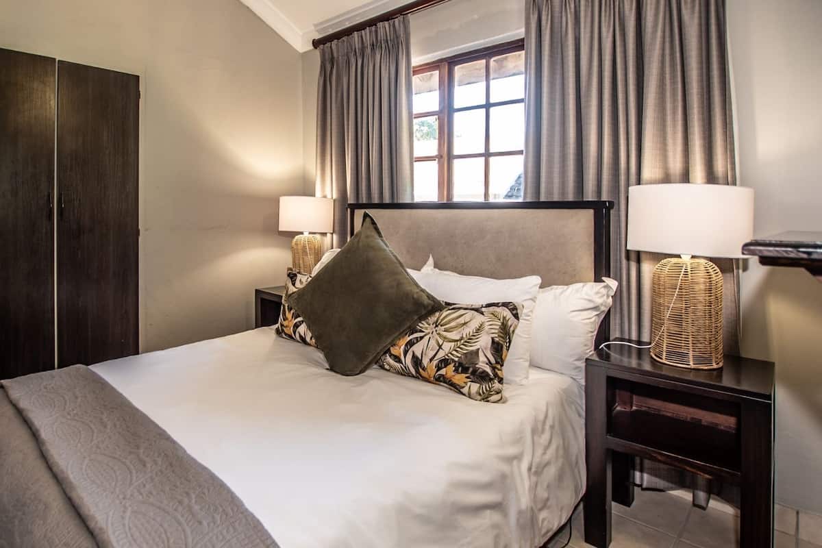 A neatly arranged hotel room with a large bed, two bedside tables with lamps, a wardrobe, and a window with curtains.