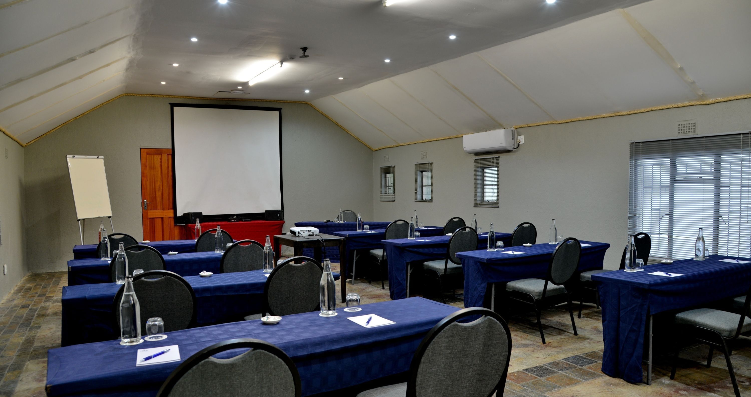 Un salón de conferencias con mesas dispuestas para una reunión, equipado con botellas de agua, blocs de notas y sillas.