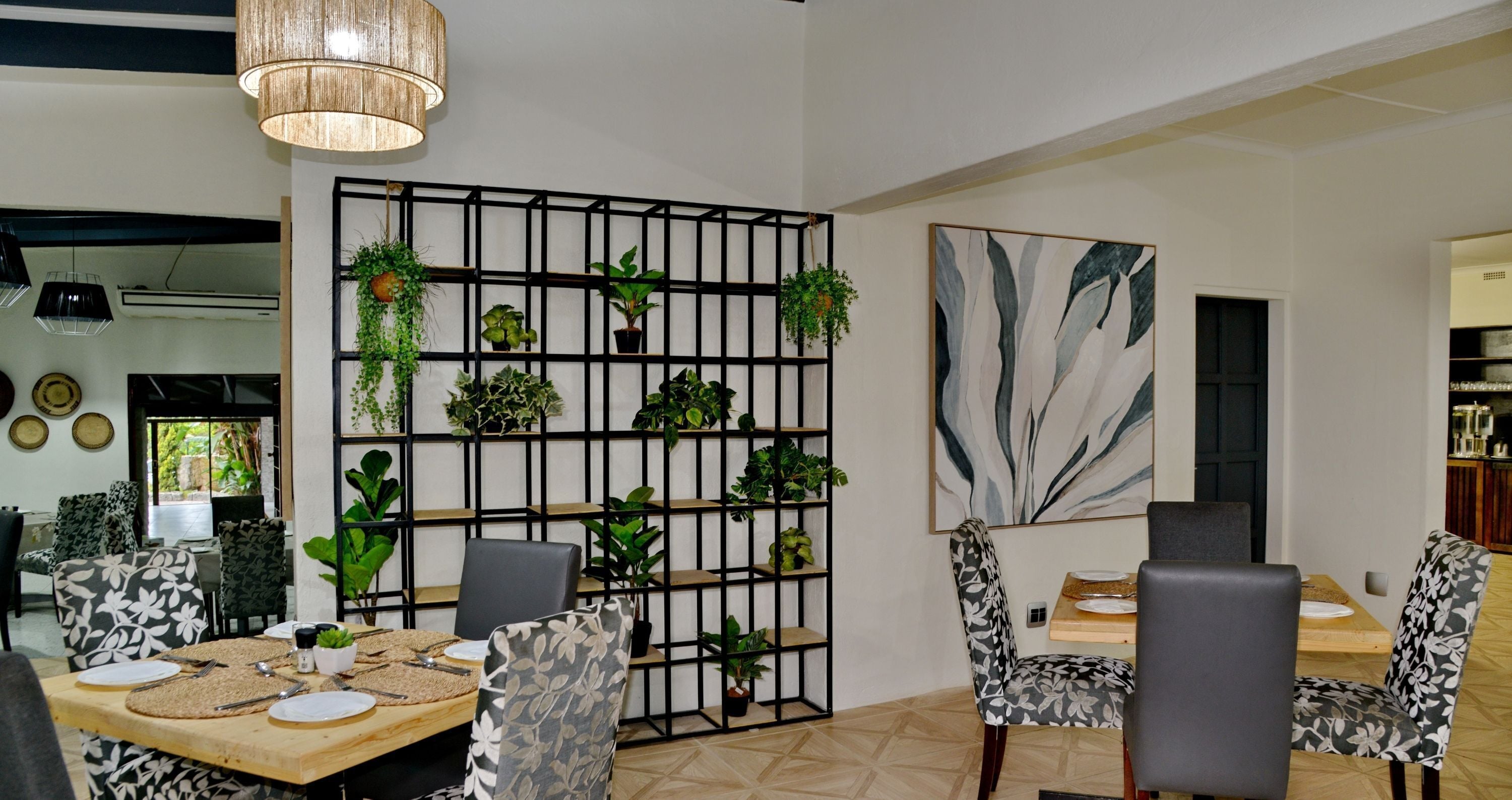 Een moderne eethoek met een houten tafel, zwart-wit gestreepte stoelen en een plantenrek van zwart metaal.