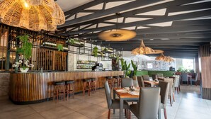 A restaurant with a bar area, wooden bar stools, and tables with chairs. - ANEW Resort White River Mbombela (Mbombela)