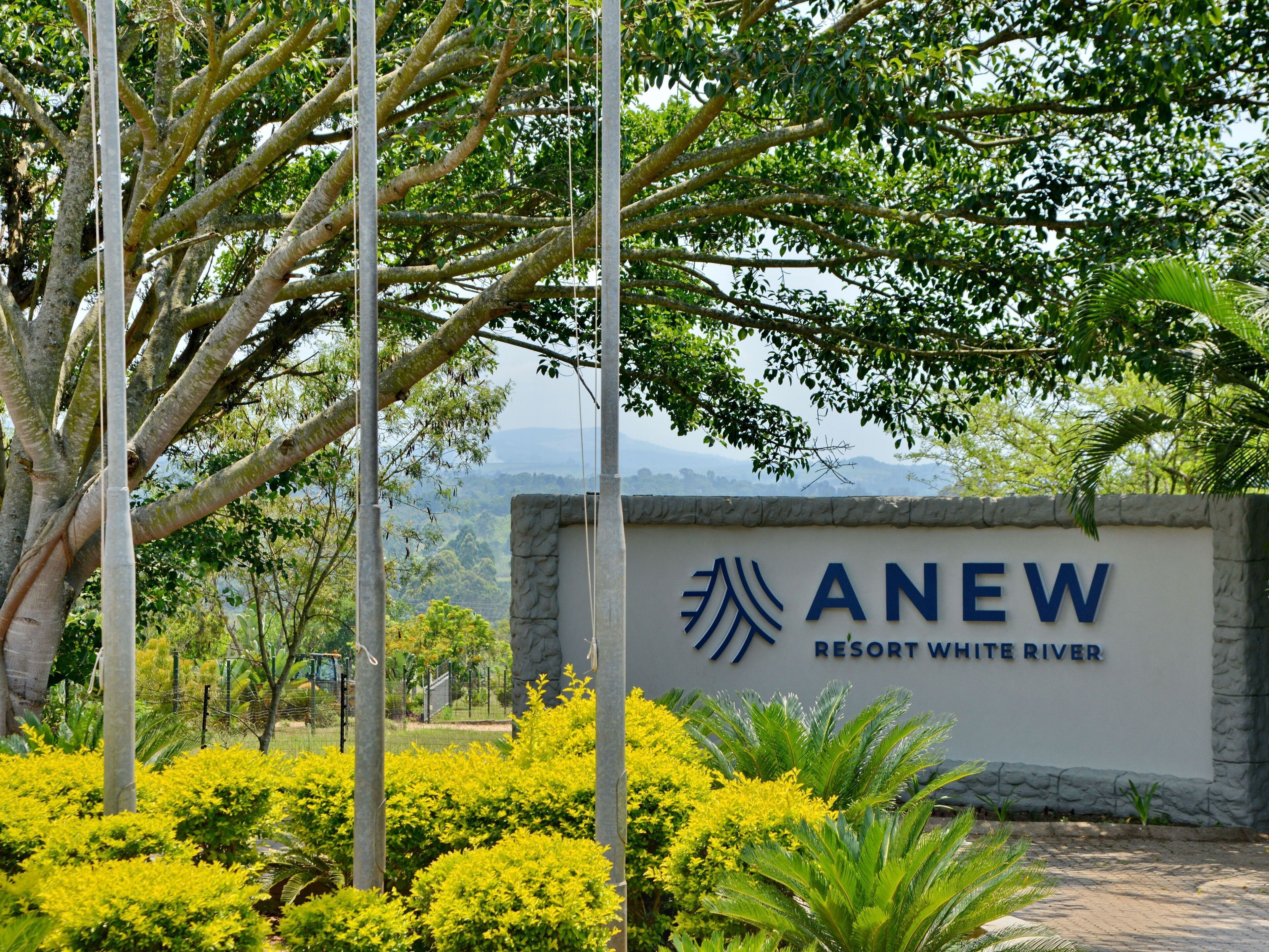 A sign for ANEW Resort White River with a stone wall and greenery around.