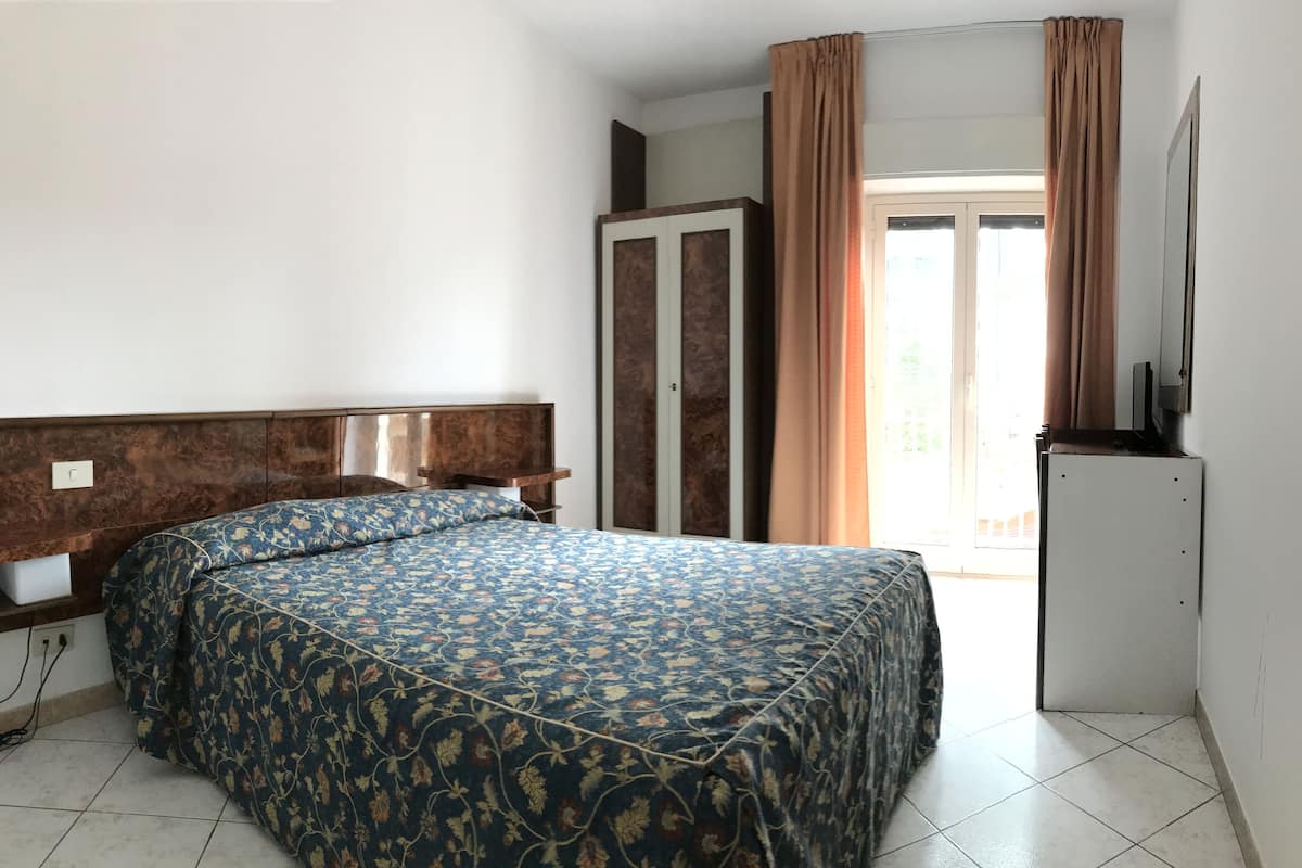 A bedroom with a bed, a wardrobe, a television, and a sliding door to a balcony.