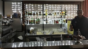 Een bar met flessen drank op de planken, een koffieapparaat en een barman.