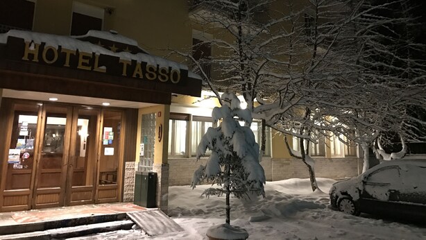 Een hotelentree met een met sneeuw bedekte bordes, een boom ervoor en een geparkeerde auto.