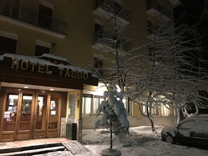 A hotel entrance with a snow-covered sign, a tree in front, and a parked car. - Hotel Tasso (Spezzano della Sila)