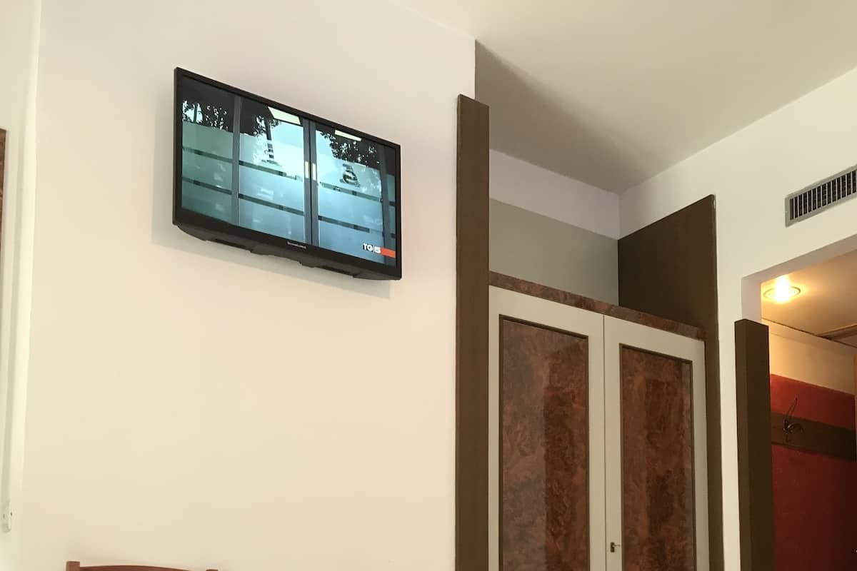 A bedroom with a bed, a TV mounted on the wall, a wooden chair, and a wardrobe.