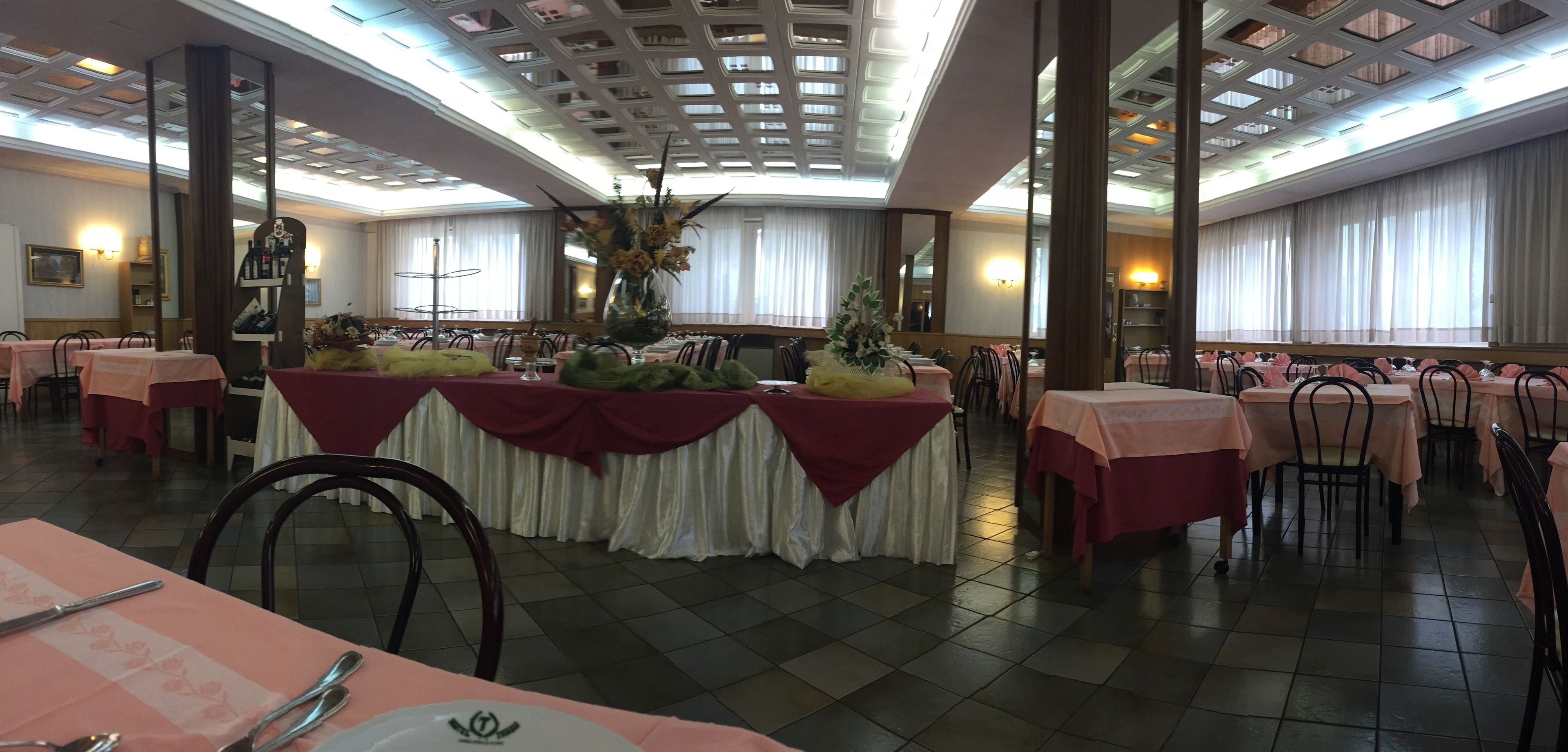 Une salle de banquet avec des tables dressées pour le repas, un arrangement floral central et un plafond haut orné d’un motif en réseau.