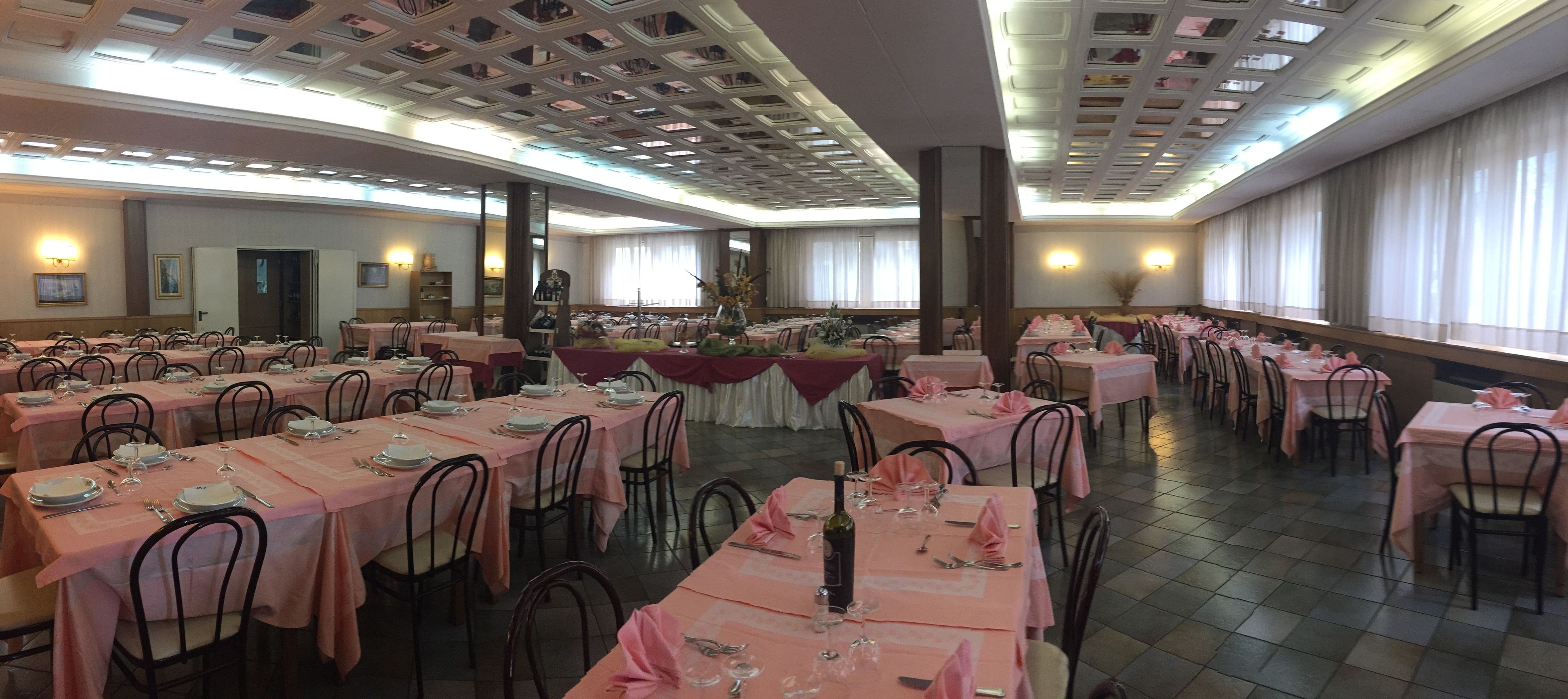 Ein Festsaal mit mehreren für das Essen gedeckten Tischen, mit einem gleichbleibenden Tischdeckenmuster und Metallstühlen.