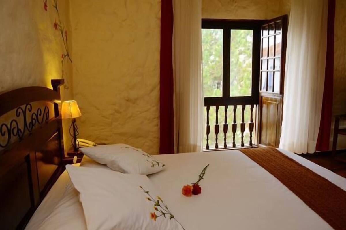 A bedroom with a bed, a nightstand, a lamp, and a window with a view of greenery.
