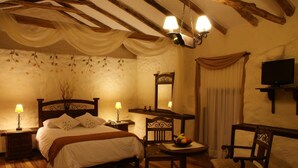 Un dormitorio acogedor con una cama de madera, dos lámparas de noche, una mesita con fruteros y un televisor sobre un soporte.