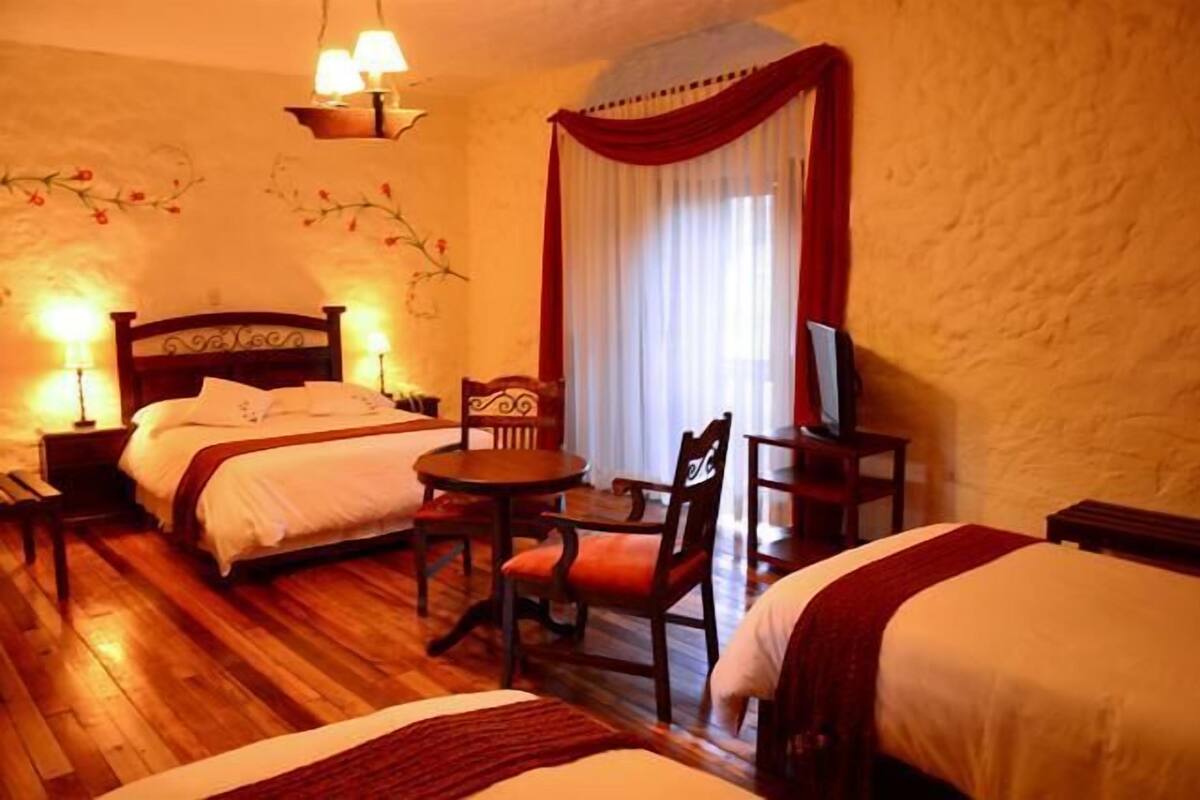 A hotel room with two beds, a small table, chairs, a TV, and a decorative wall.