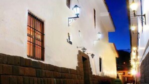 Una calle estrecha con edificios blancos, un muro de ladrillo y una persona alejándose.