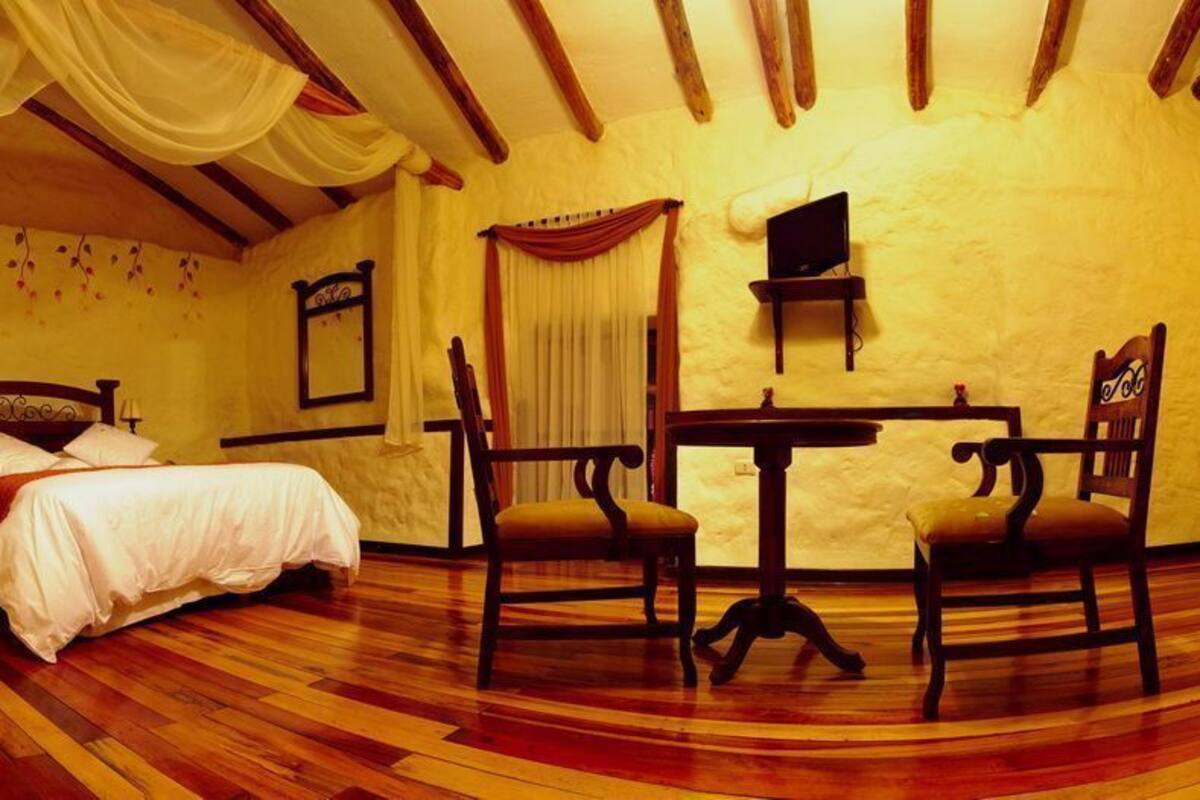 A room with a bed, two chairs, a table, and a television.