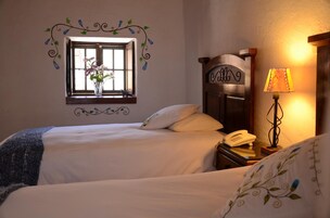 A hotel room with two beds, a window with a vase of flowers, a lamp, and a telephone on the nightstand.