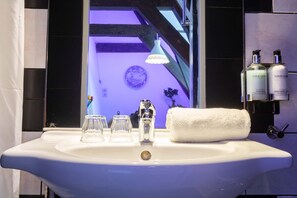 A bathroom with a white sink, three glass tumblers, a white towel, and two bottles of hand soap. - Tulip Of Amsterdam (Amsterdam)
