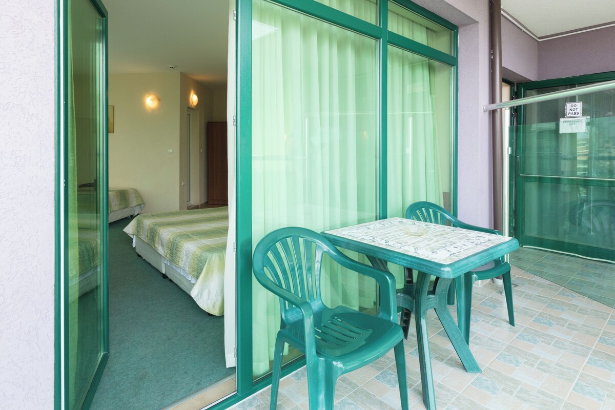 A room with a bed, a table with chairs, and a sliding glass door.