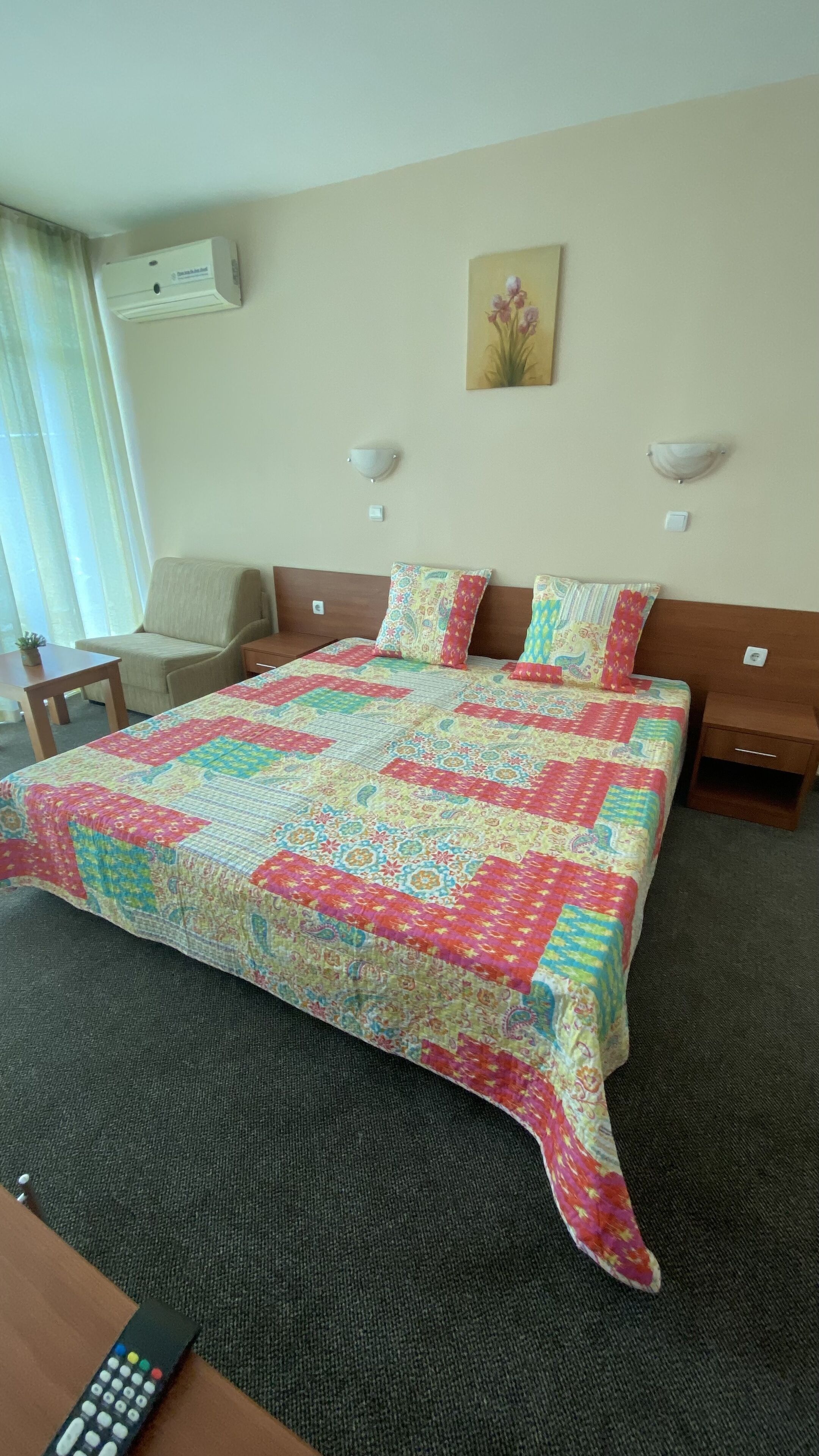 A hotel room with a bed, a chair, a nightstand, a lamp, and a painting on the wall.