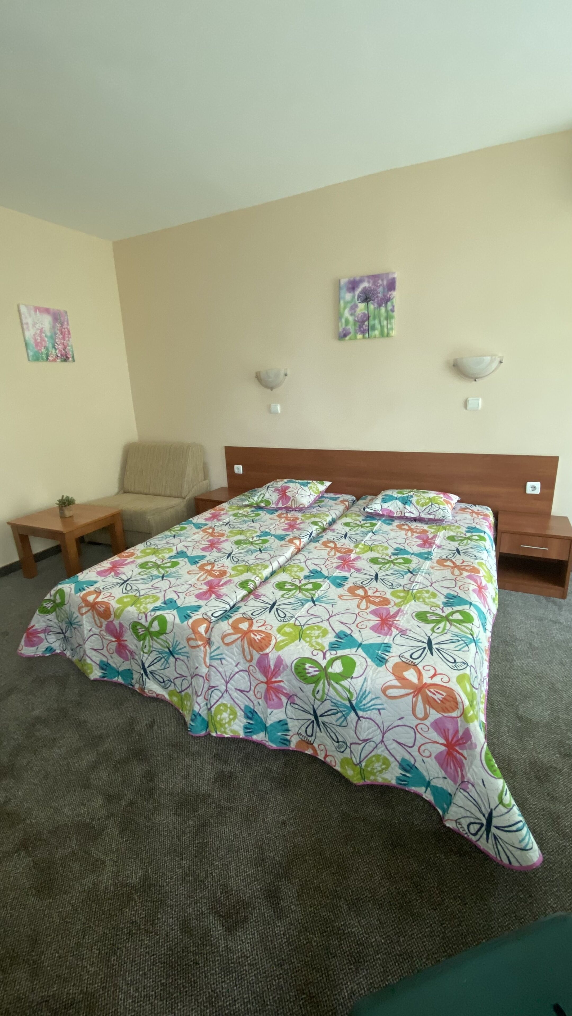 A hotel room with a bed, a chair, a small table, and two wall-mounted lamps.