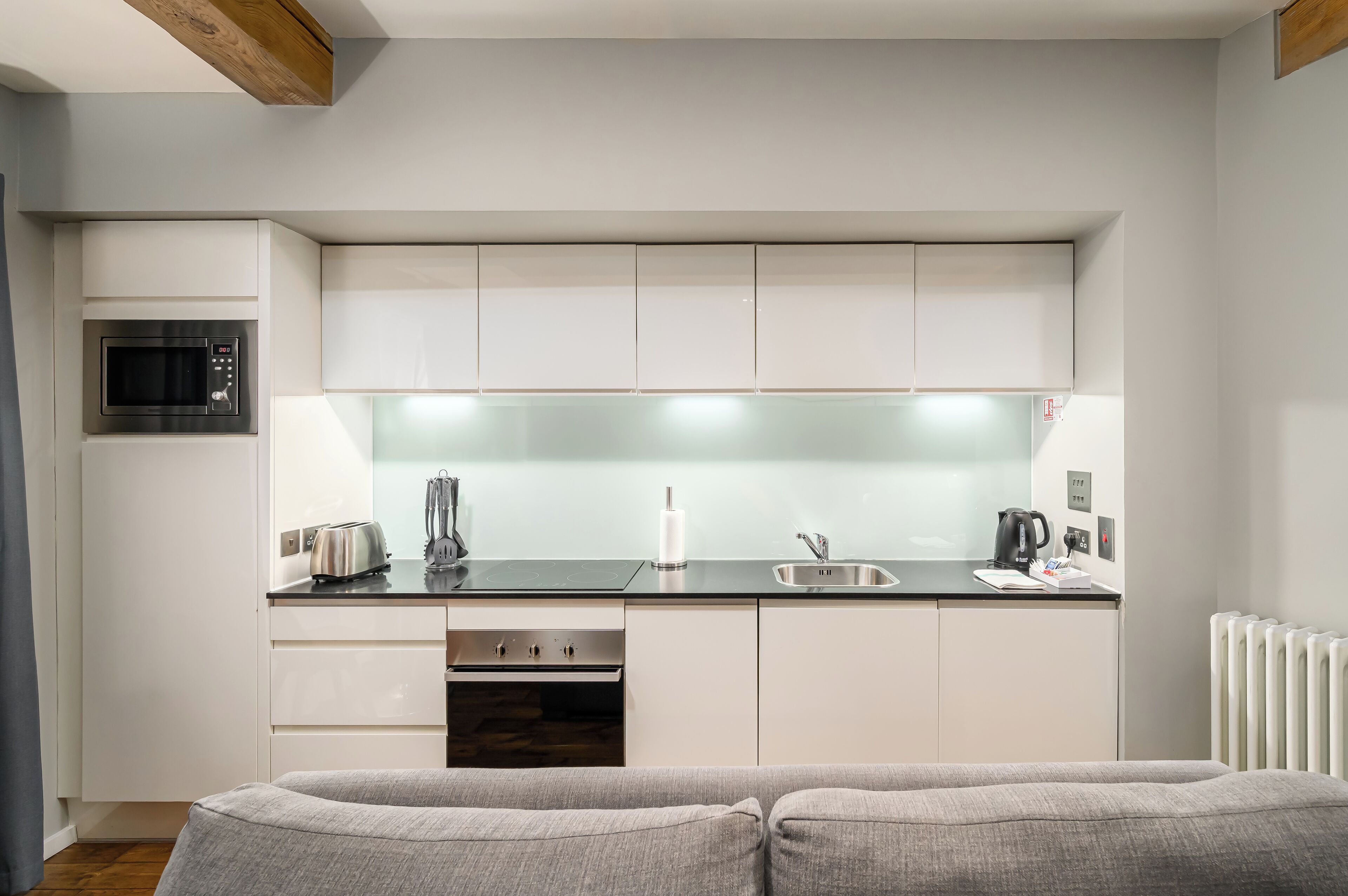 A compact kitchen with white cabinets, a microwave, a toaster, and a kettle.