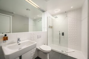 A modern bathroom with a white sink, toilet, and glass-enclosed shower. - Destiny Scotland - The Malt House Apartments (Edinburgh)
