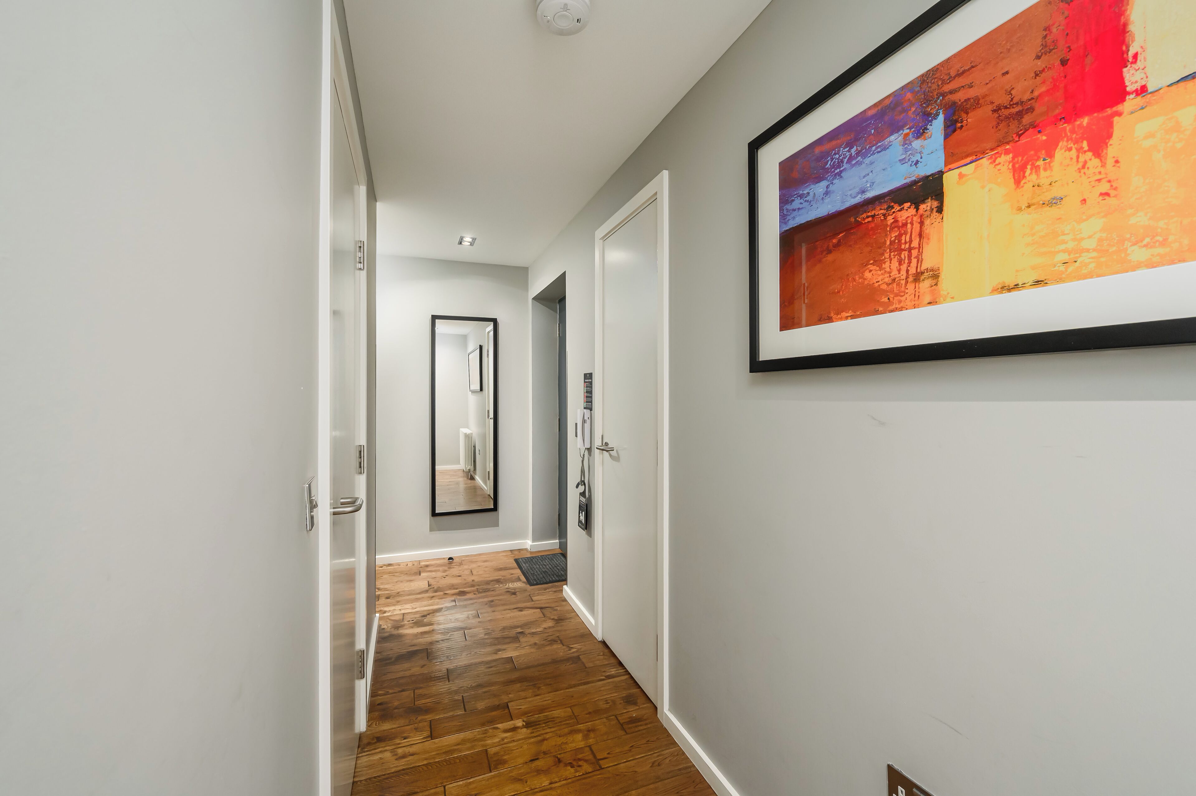 A hallway with a wooden floor, white walls, and a framed abstract painting.