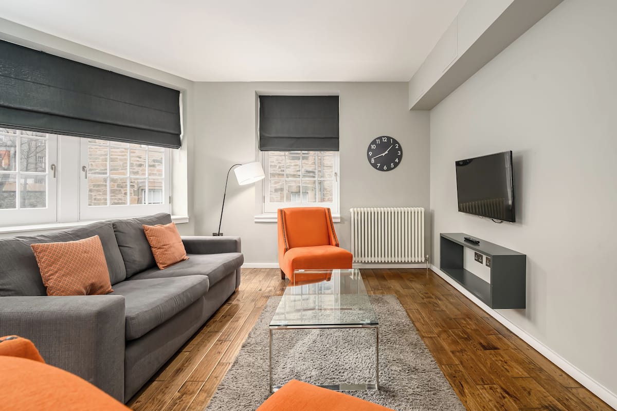 A modern living room with a grey sofa, orange armchair, and a glass coffee table.