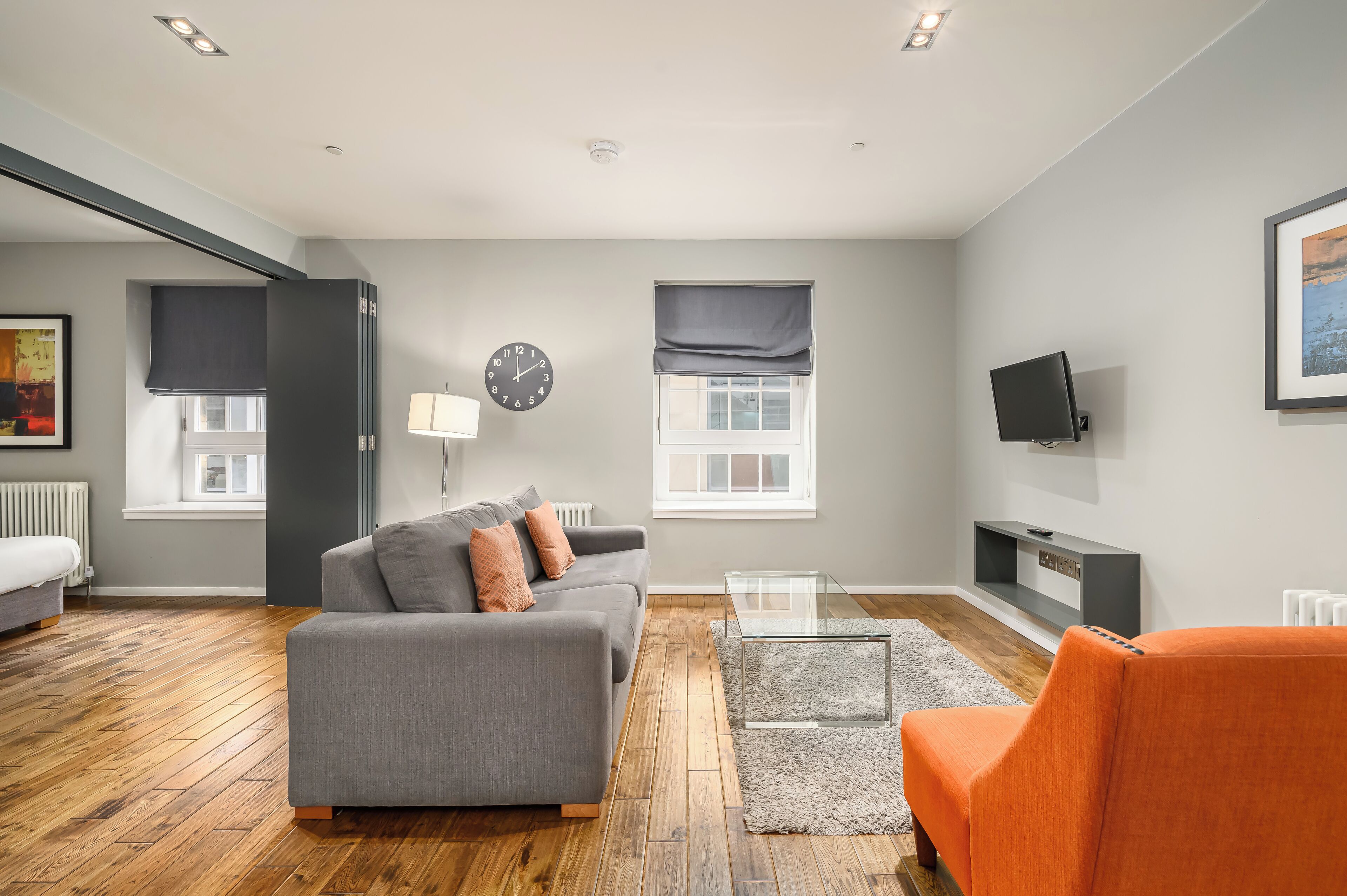 Ein modernes Wohnzimmer mit einem grauen Sofa, einem orangefarbenen Sessel und einem Glastisch.