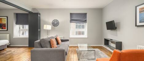 Ein modernes Wohnzimmer mit einem grauen Sofa, einem orangefarbenen Sessel und einem Glastisch.