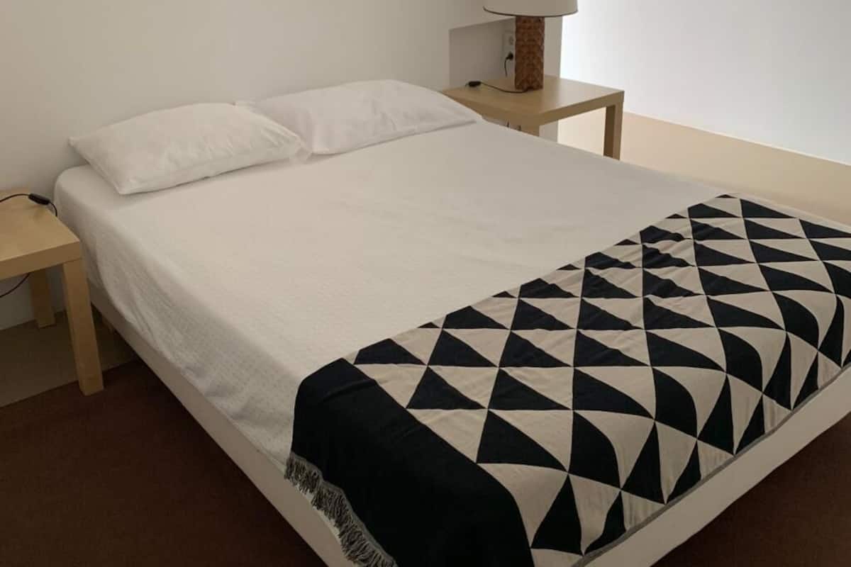 A neatly made bed with a geometric-patterned blanket, a bedside lamp, and a small wooden nightstand.