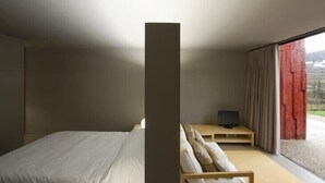 Een moderne slaapkamer met een bed, een televisie op een houten standaard en een groot raam met gordijnen.