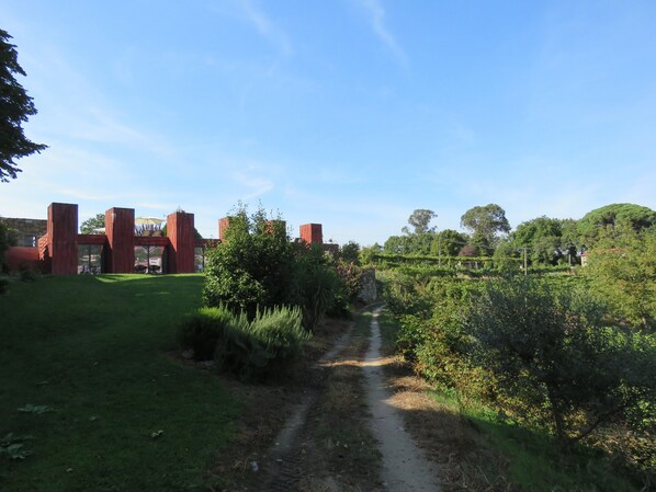 Un sentier rural qui traverse un jardin luxuriant, bordé d’un mur de pierres et agrémenté de constructions en bois rouge.