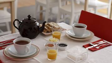 Una escena de desayuno con tetera, tazas, tostadas, mantequilla, mermelada y terrones de azúcar sobre una mesa.