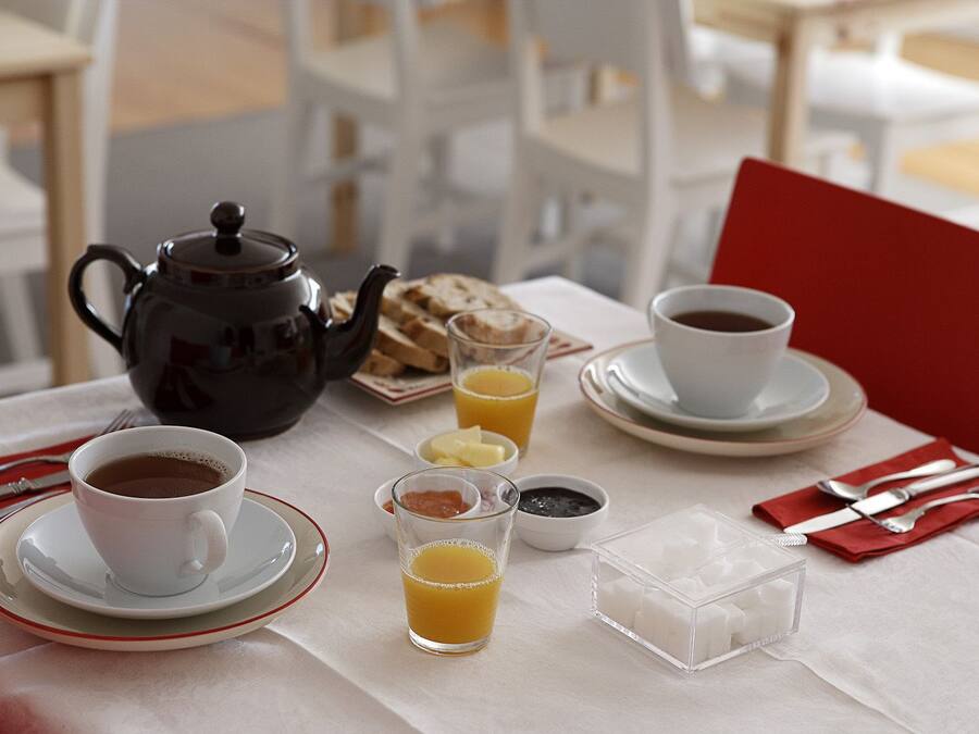 A breakfast setting with a teapot, cups, toast, butter, jam, and sugar cubes on a table.