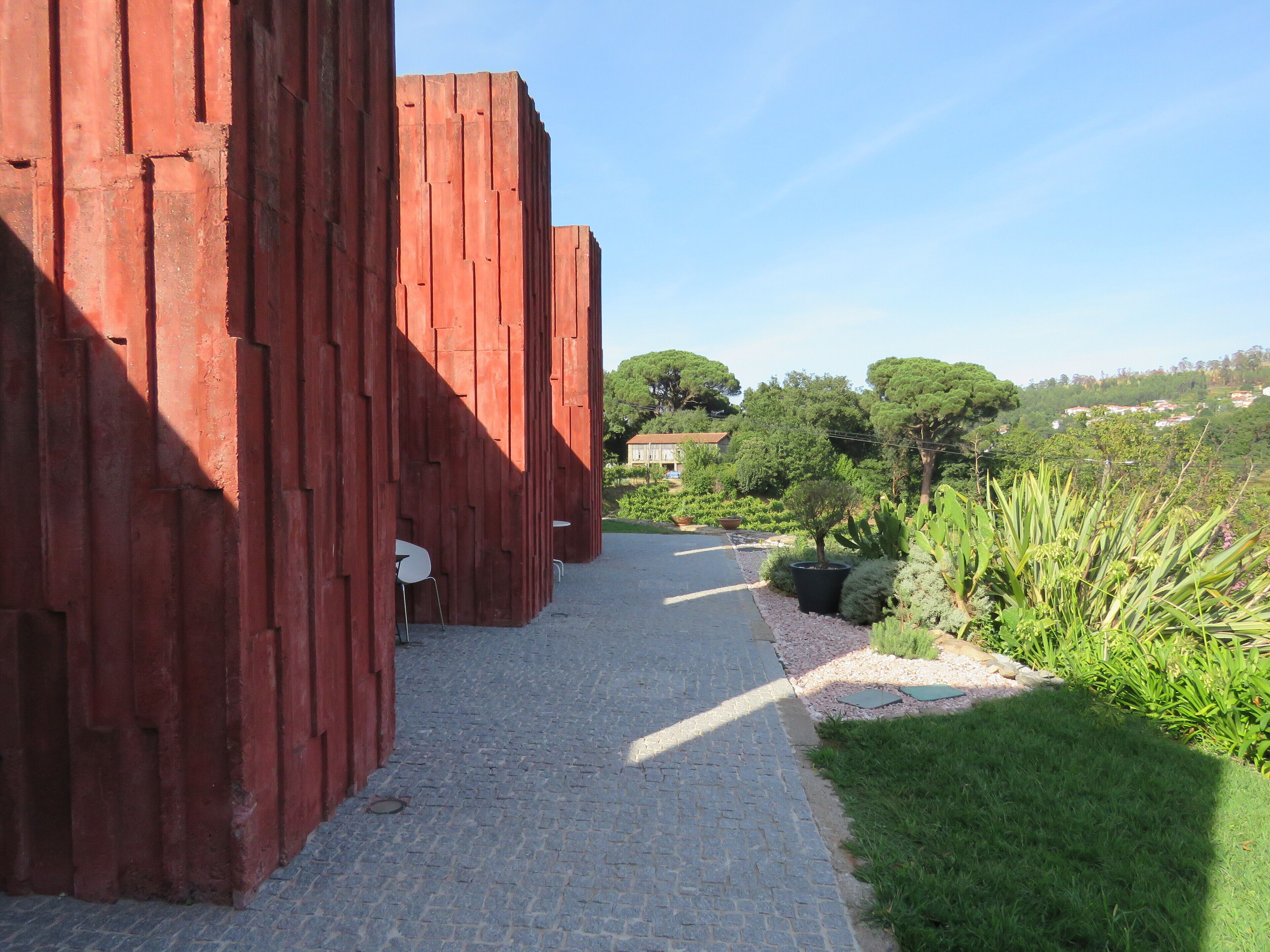 A cobblestone pathway leading to a red wooden structure with white chairs.