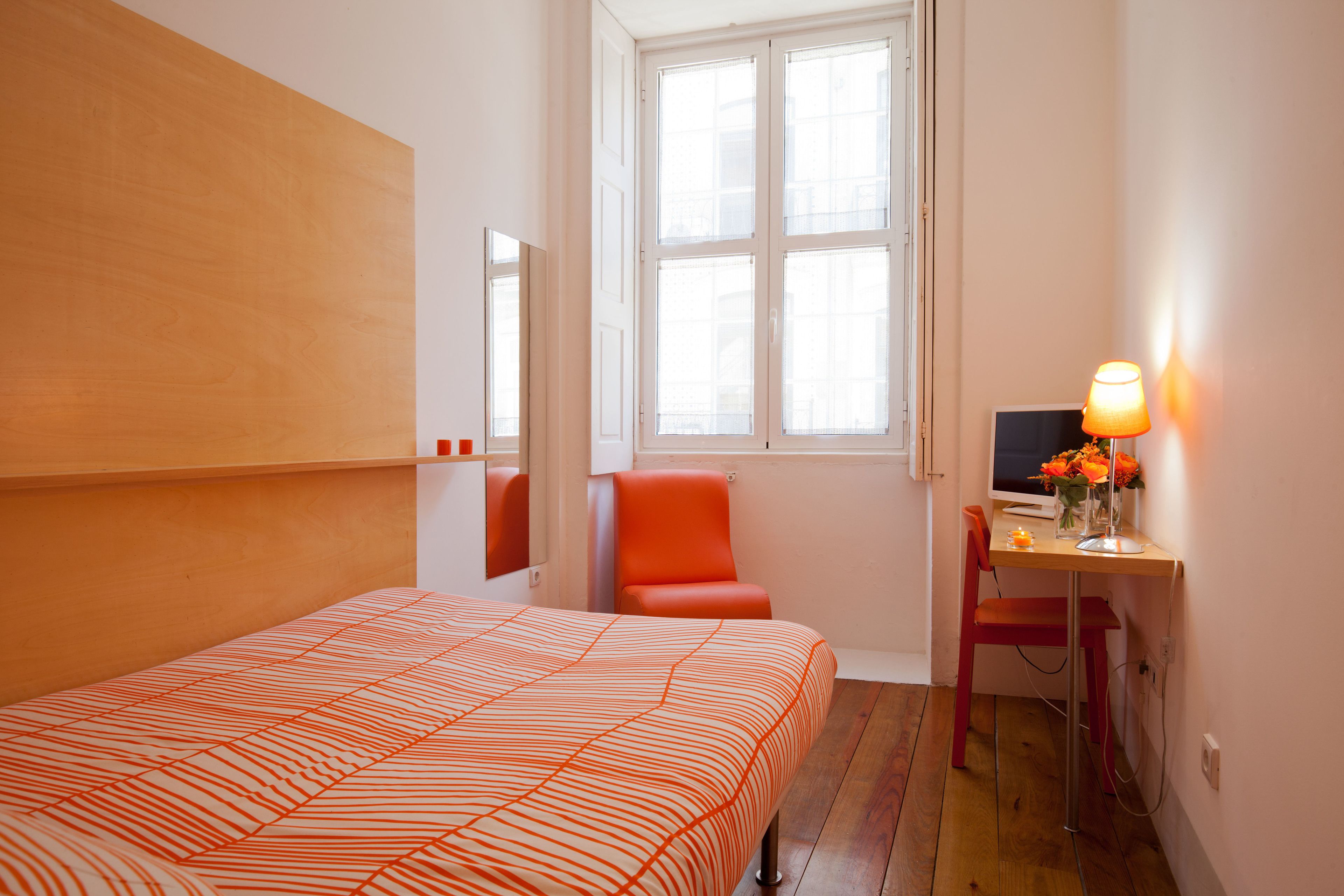 A hotel room with a bed, a desk with a computer, a chair, and a window with natural light.
