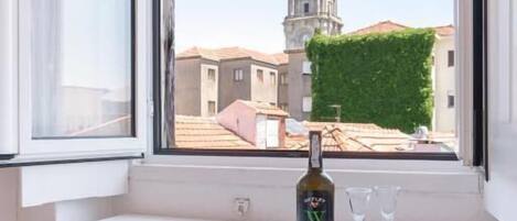 A window seat with a bottle and glasses, overlooking a building with a tower.