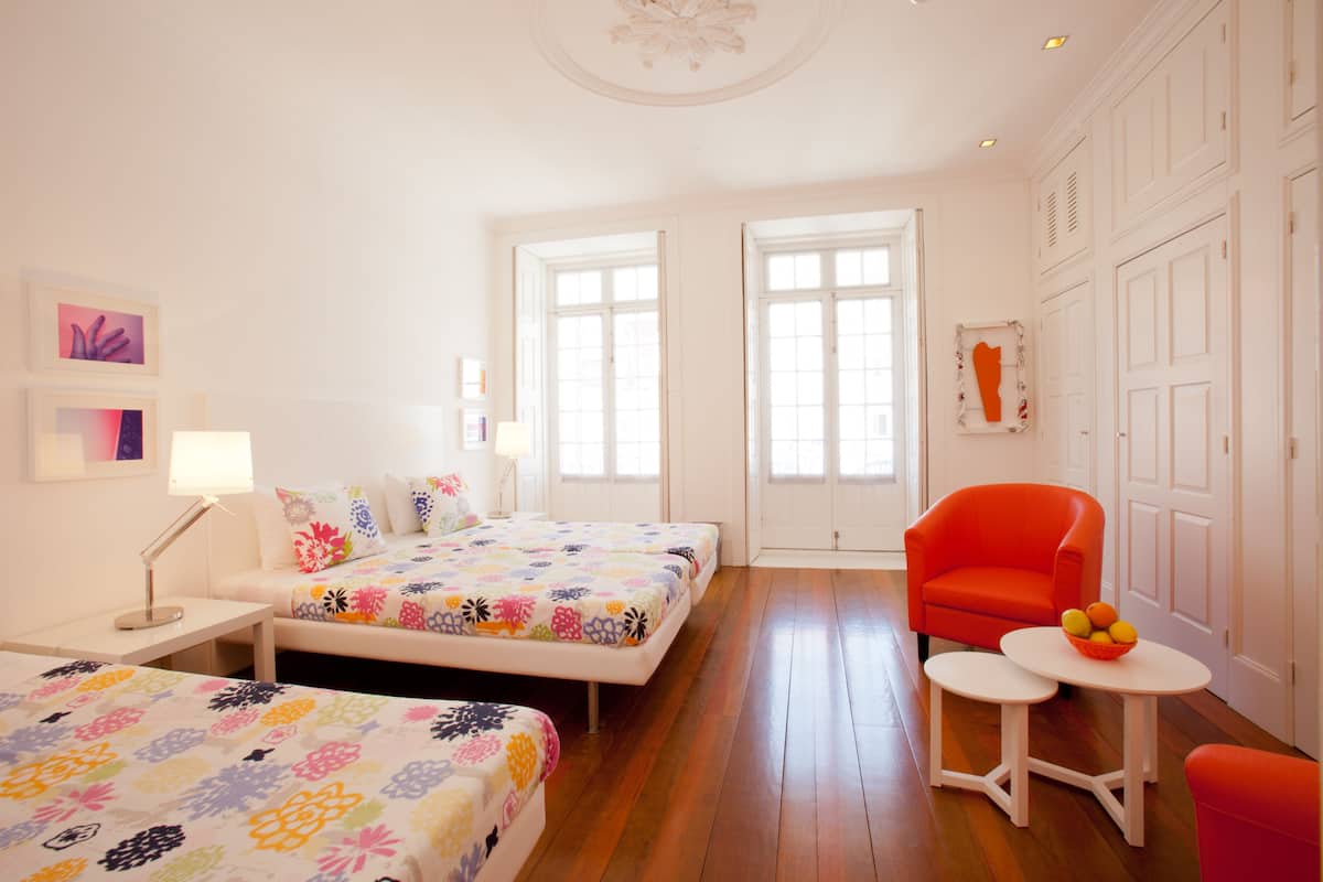 A hotel room with two beds, a small table with fruit, and a bright, airy design with large windows.