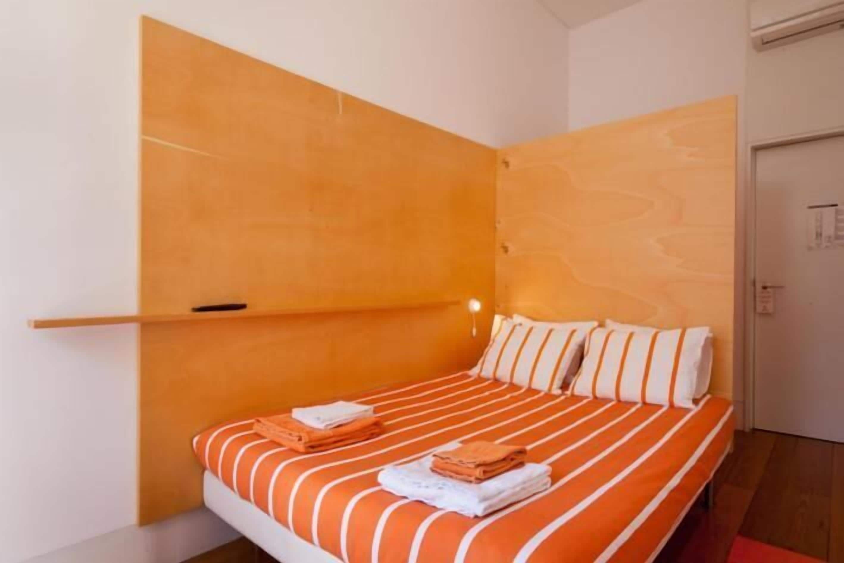 A bedroom with a bed, orange and white striped bedding, a wooden headboard, and a red rug.