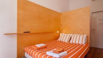 Une chambre à coucher avec un lit, une literie à rayures orange et blanches, une tête de lit en bois et un tapis rouge.